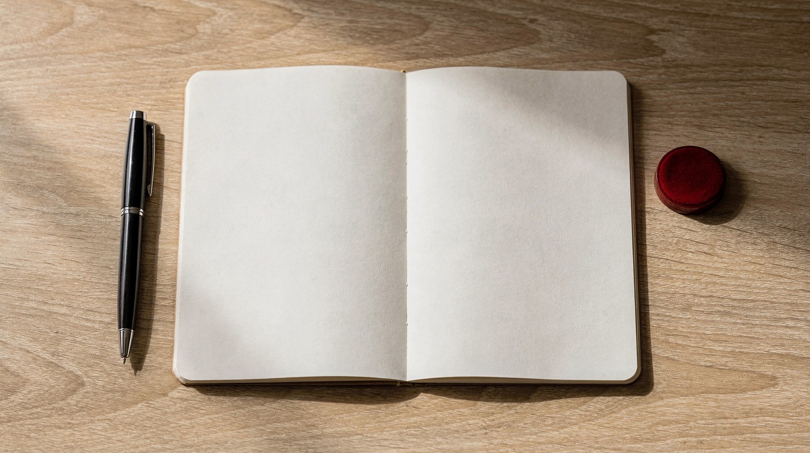 Caderno aberto com página em branco, caneta e carimbo de tinta vermelha sobre uma mesa de madeira
