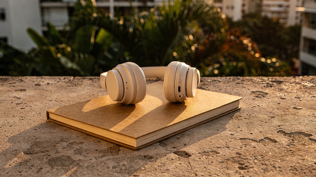 Fones de ouvido sobre caderno fechado em varanda de apartamento, folhagem tropical ao fundo, luz dourada do fim de tarde