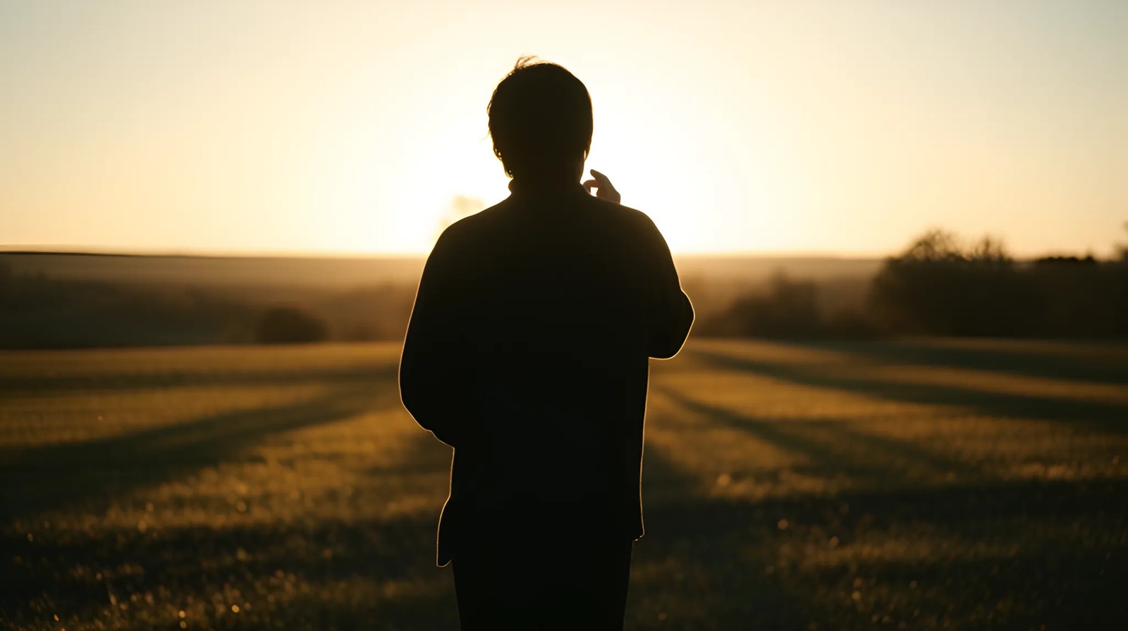 Silhueta de uma pessoa ao longe, ouvindo atentamente em um campo aberto durante o pôr do sol